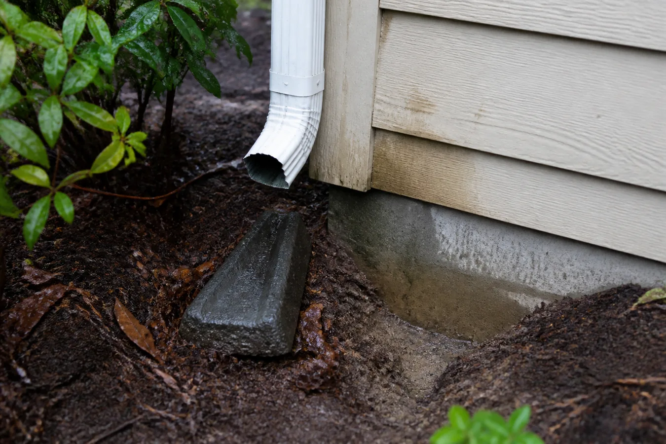 Illustrated disconnected downspout and splash block at a house corner.